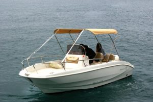 Una barca open con il tendalino beige aperto e due persone al posto di guida