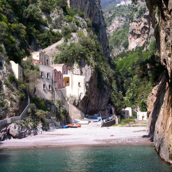 Spiaggetta in fondo a una gola, tra case sulla roccia e barche in secca