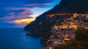 Le case illuminate di Positano sul pendio, sotto un cielo viola e arancio al tramonto